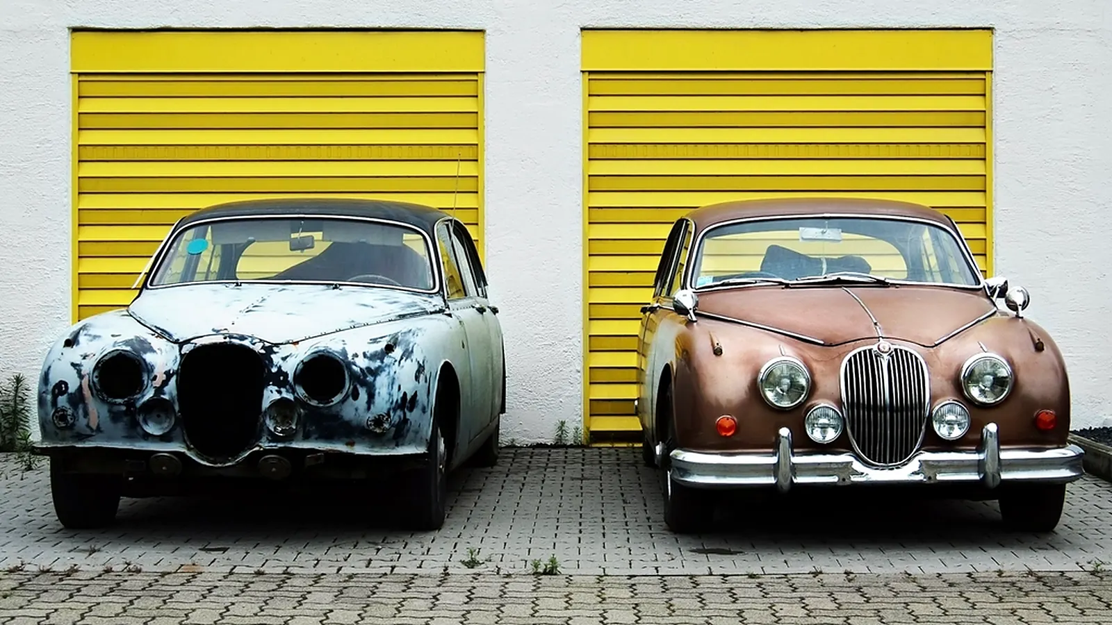 Du seni klasikiniai automobiliai prie geltonų garažo vartų