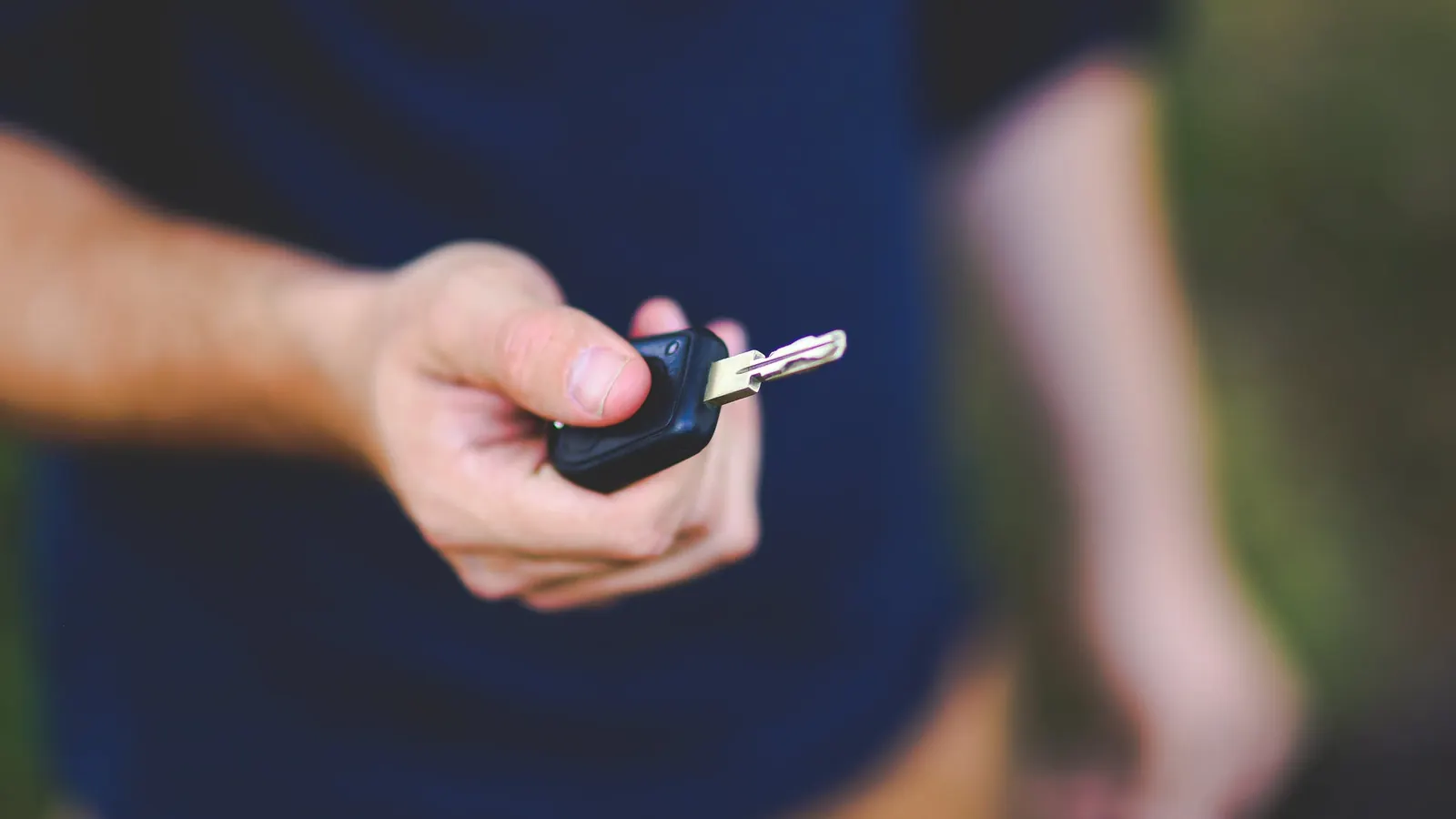 Žmogus ištiesęs ranką perduoda automobilio raktelį naujam savininkui